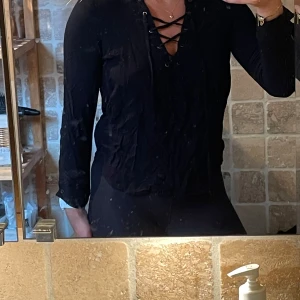 Svart henley med snörning Forever 21 - Svart henley-skjorta från Forever 21 med lång ärm och snygg snörning framtill vid halsen. Skjortan har en smickrande passform och är perfekt för dig som gillar en stilren men ändå trendig look.