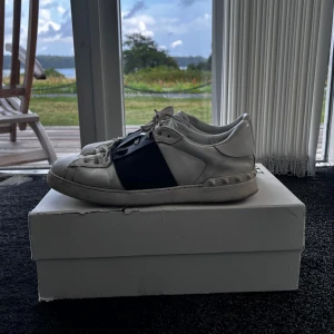 Valentino skor - Säljer ett par vita Valentino Open sneakers med bred svart rem över mitten. Skorna har snörning, rund tå och platt sula. Storlek 44, allt og ingår, skick 7/10, pris går att diskutera✅