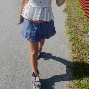 Blå volangkjol  - Supersöt blå kortkjol med plisserad volangkant och klassisk knapp- och gylf framtill. Kjolen har bälteshällor och en avslappnad passform som ger en cool vibe. Perfekt att styla med boots eller sneakers för en trendig look. Är omsydd från en lång kjol, till en kort med volang för att skapa en mer trending och unik look. Kan vikas ner i midjan så det blir ett rosa band vilket gör att storleken blir lite mindre än M! Billigt, snyggt och miljövänligt! 