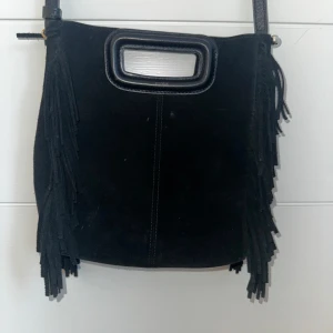 SVART MAJE VÄSKA  - Svart axelväska i mocka med coola fransar längs sidorna och ett rektangulärt handtag upptill. Väskan har lång axelrem och en stilren, enkel design som passar till många outfits.  Den har använts en del men har inga skador utom att texten har fadat lite där det står make