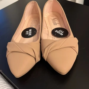 Beige ballerinaskor med spetsig tå från Shein - Stilrena beige ballerinaskor från Shein med bred passform och spetsig tå. Skorna har en snygg twistad detalj framtill och är gjorda i syntetmaterial. Perfekta för dig som vill ha en enkel men trendig look. Storlek 40 men jag har 39 och de passar mig.