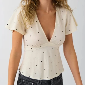Prickig v-ringad blus från ginatricot  - Supersöt ljusbeige blus från Primark med svarta prickar, djup v-ringning och korta, vida ärmar. Blusen har en feminin passform med lätt utsvängd nederdel och knyt i ryggen. Perfekt för dig som gillar en lekfull och trendig stil. Pris kan diskuteras 💕