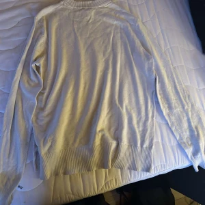 Ljusbeige stickad tröja från H&M - En stilren ljusbeige stickad tröja från H&M i storlek S. Tröjan har ribbade muddar vid hals, ärmslut och nederkant. Perfekt för lager-på-lager och funkar till många olika outfits.
