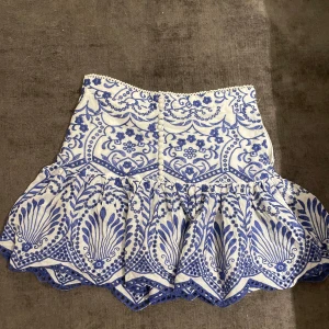 Vit och blå mönstrad kjol från Zara - Superfin kort kjol från Zara i vitt med blått broderat mönster. Perfekt som somriga plagg med mycket detaljer. 