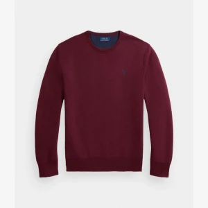 Vinröd tröja från Polo Ralph Lauren - Vinröd tröja från Polo Ralph Lauren med rund halsringning och diskret broderad logga på bröstet. Klassisk passform och långa ärmar, perfekt för lager-på-lager. Tillverkad i mjukt material som känns skönt mot huden.
