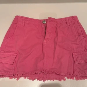 Rosa kortkjol med fransig kant - Snygg rosa kortkjol med fransig nederkant och coola fickor på sidorna. Kjolen har dragkedja och knapp framtill. 💕💕