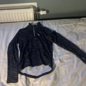 Randig tränings-tröja från Trimtex - Säljer en svart och grå randig långärmad tränings-tröja från Trimtex. Tröjan har half zip framtill och är tillverkad i ett lätt och ventilerande material av polyester och elastan. Perfekt för löpning eller annan träning under kyligare dagar. jätte skön 