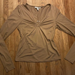 Beige långärmad topp - Säljer en beige långärmad topp från H&M i stretchigt material. Toppen har v-ringning med snygg silvrig detalj i mitten framtill. Perfekt för dig som gillar stilrena plagg!💕
