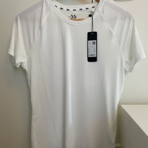 Vit sportig t-shirt från 157 - Vit t-shirt från 157 med enkel och clean design. T-shirten har korta ärmar, rund halsringning och är gjord i ett lätt och svalt material som passar perfekt till träning. Liten logga på ärmen och bekväm passform.
