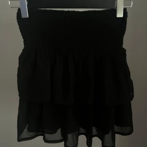Svart volangkjol från KappAhl - Supersöt svart kortkjol från KappAhl med bred smock i midjan och dubbla volanger. Kjolen är luftig och är perfekt att ha till soliga och varma dagar! Passar till allt. 
