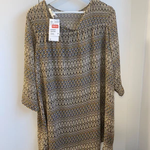 Mönstrad klänning från H&M - Klänning från H&M med grafiskt mönster i svart, gult och beige. Klänningen har trekvartsärm och en lös passform. Materialet är lätt och känns skönt mot huden, perfekt för dig som gillar unika prints och bekväma plagg. Har även ett tunnt svart innertyg, se sista bilden. Går att använda som tunika eller kort klänning beroende på storlek.
