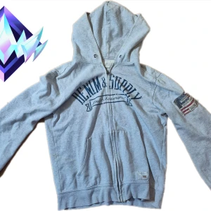 Grå hoodie från Ralph Lauren Denim & Supply - Grå hoodie med dragkedja från Ralph Lauren Denim & Supply. Stor huva, känguruficka och tryck framtill. På ena ärmen finns en patch med amerikansk flagga och broderad text. Mjuk bomullskänsla, perfekt för chill dagar.