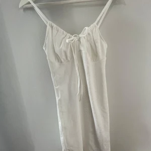 Vit klänning från SHEIN - Superfin vit klänning från SHEIN i storlek XS. Klänningen har smala axelband, knytning framtill och ett diskret hålmönster i tyget. Tillverkad i mjuk polyesterblandning med lite stretch för en bekväm passform. Väldigt bra kvalitet för att vara från shein, like bra som något plagg från något annat ställe. Jättefin till sommaren🤍