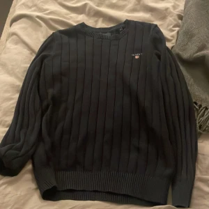 Svart ribbad tröja från Gant XS - Säljer en svart ribbstickad tröja från Gant i storlek XS. Tröjan har rund halsringning, diskret Gant-logga på bröstet och är tillverkad i mjuk bomull. Perfekt för dig som gillar klassisk och stilren look.