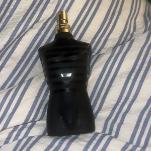 Jean Paul Gaultier Le Male Le Parfum - Säljer en ikonisk parfymflaska från Jean Paul Gaultier, Le Male Le Parfum. Flaskan är formad som en manlig torso i mattsvart glas med blanka svarta ränder och har en guldfärgad spraykork. Volymen är 125 ml. Där mitt pekfinger är där är parfymen nästan som ny 