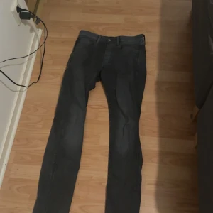 Mörkgrå jeans från G-Star RAW - Säljer ett par mörkgrå jeans från G-Star RAW med klassisk femficksdesign och snyggt läderpatch bak i midjan. Jeansen har slim passform och raka ben, perfekta för en clean och modern look. Materialet är mjukt och stretchigt för extra komfort. Storlek W30/L34