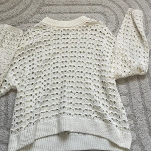 Vit stickad tröja med hålmönster - Vit stickad tröja från Cubus i storlek 158/164. Tröjan har ett snyggt hålmönster över hela plagget och ribbade muddar vid hals, ärmslut och nederkant. Perfekt för lager-på-lager och ger en fräsch look till din outfit.