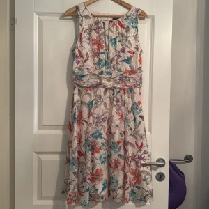 Blommig sommarklänning från Esprit - Superfin blommig klänning från Esprit i ljusa färger med inslag av rött, blått och lila. Klänningen är ärmlös, har en markerad midja och lätt utställd kjol. Perfekt för varma dagar och har dragkedja i ryggen.