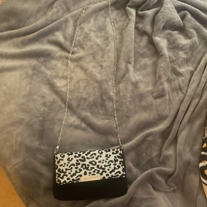 Svart axelväska med leopardmönster - Snygg svart axelväska med silverfärgad kedja och  svartvitt leopardmönster. köpte den second hand men har aldrig använt och den är bra kvalite. skriv gärna om ni har frågor🥰