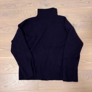 Mörkblå stickad polotröja - Mysig mörkblå stickad polotröja med hög krage och lång ärm. Tröjan har en loose fit och är perfekt för kyliga dagar. Enkel och stilren design som passar till det mesta. Materialet är tjockt och ger en skön känsla.