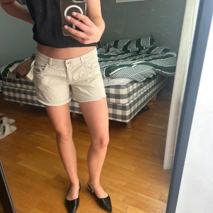 Beige shorts med rå kant - Snygga beige shorts med rå, fransad kant och klassisk femficksmodell. De har låg midja och stängs med knapp och dragkedja. Perfekta för varma dagar och enkla att matcha med allt. Materialet känns mjukt och skönt mot huden.