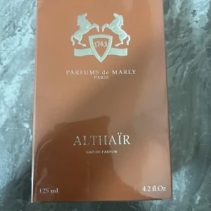 Parfums de Marly Althaïr 125ml - Exklusiv parfym från Parfums de Marly, Althaïr, 125 ml Eau de Parfum. Flaskan är matt brun med silverdetaljer och har en elegant, fyrkantig form med två upphöjda hästar och skölden '1743' på framsidan. Lyxig och stilren design med metallisk silverkork.