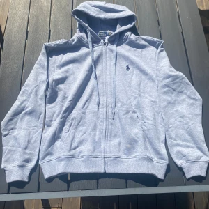Ljusgrå hoodie från Polo Ralph Lauren - Marinblå hoodie med dragkedja från Polo Ralph Lauren. Hoodien har en röd logotyp på bröstet och två fickor fram. Använd 7 gånger, tvättad i efterhand