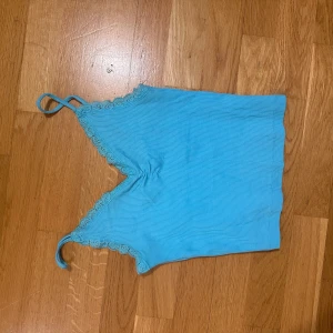 Ljusblå ribbad linnetopp med spets - Supersöt ljusblå linnetopp med smala axelband och v-ringning. Toppen har ribbad struktur och fina spetsdetaljer längs kanterna. Perfekt för varma dagar eller att styla lager på lager.