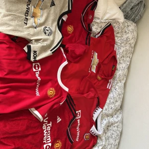 Manchester United fotbollströjor herr - Samling av Manchester United fotbollströjor med spelarnamn som Ronaldo, Rashford, Garnacho och Lukaku. Tröjorna är kortärmade, i klassiskt röd och en i ljusbeige med svarta detaljer. Broderad klubbmärke, sponsorloggor och tryckta namn/nummer. Perfekt för United-fans! Skriv om man vill diskutera pris! Man kan köpa alla eller kanske bara 1? Det är olika storlekar i alla. 