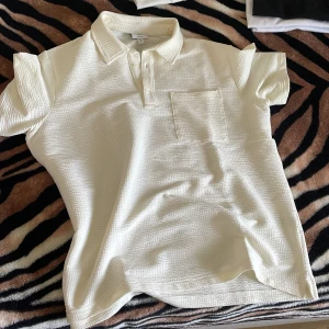 Vit pikétröja i strukturerad bomull - Snygg vit pikétröja från H&M i strukturerad bomull. Klassisk krage, kort ärm och bröstficka ger en clean och fräsch look. Perfekt till jeans eller shorts när du vill vara casual men ändå stilren.