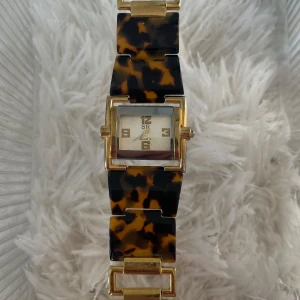Klocka med sköldpaddsmönster och guld - Stilren klocka med fyrkantig urtavla i guld och armband i sköldpaddsmönstrad plast. 
