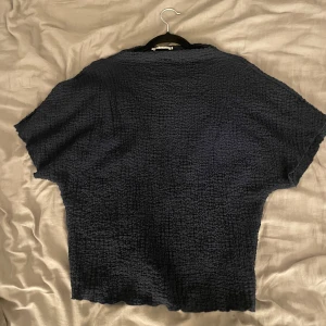 Mörkblå strukturerad topp - En mörkblå topp med korta ärmar och boxig passform. Tyget är strukturerat och ger en cool, lite vågig effekt. Perfekt för dig som gillar en enkel men ändå unik look. Toppen är croppad och har en avslappnad vibe.