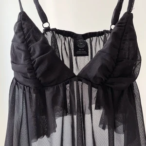 Svart topp - Supersöt svart top från Urban Outfitters i mesh med tunna axelband och v-ringad byst. 🌸Perfekt för dig som gillar en edgy och trendig stil.