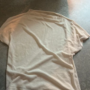 Beige t-shirt från Gina Tricot - En basic beige t-shirt från Gina Tricot i storlek S. T-shirten har klassisk passform med korta ärmar och rund hals. Perfekt att matcha med jeans eller kjol för en clean och enkel look.