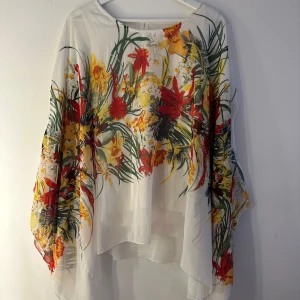 Za italia blus  - Vit Za italia blus med ett färgstarkt blommönster i rött, gult och grönt. Blusen har en lös passform och en asymmetrisk fåll som är längre baktill. Det finns en innertröja i blusen som funkar som ett linne så de inte blir genomskinlig. Innertröjan är lite defekt i armhålorna dör en söm har släppt, vänligen se bild 4 och 5. Men inget som syns då det är innetröjan. Blusen är annars i mycket fint skick. Storlek S/M, men skulle säga något stor i storlek.