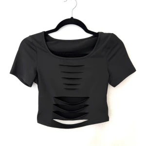 Svart croppad topp med slits - Svart croppad topp från SHEIN med korta ärmar och coola slitsdetaljer framtill. Toppens stretchiga material ger en tight passform och den har en rund halsringning. Perfekt för dig som vill sticka ut med en edgy stil.