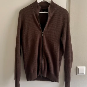 Massimo Dutti - Säljer en brun kofta från Massimo Dutti i extrafin bomull. Tröjan har hel dragkedja, ribbad krage och i ribbat mönster. Passar perfekt för finare tillfällen. ”Mörk Bild”