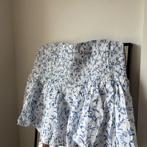 Vit och blå blommig kortkjol H&M - Supersöt ny kortkjol från H&M i vitt med blått blommönster. Kjolen har smockad midja som ger flexibel passform. 