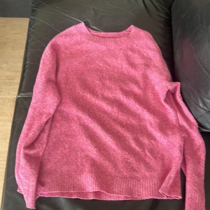 Rosa stickad tröja med rund hals - En mysig rosa stickad tröja med rund hals och långa ärmar. Tröjan har en enkel och stilren design med ribbade muddar vid ärmslut och nederkant. Perfekt för lager-på-lager och chill dagar.