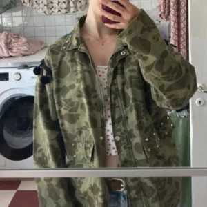 Zara jacka med broderier - Unik grön camouflage jacka med färgglada broderier och mönster på ryggen. Jackan har nitar på kragen och fickorna, samt svarta fransdetaljer på ärmarna (några av bollarna har ramlat av, se bild). Oversized passform och långärmad.