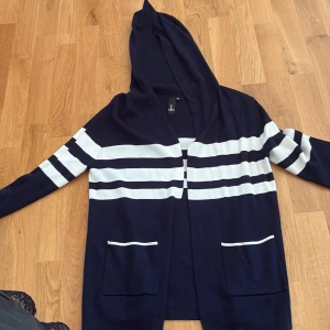 Marinblå randig hoodie-kofta från Cienna - Snygg marinblå kofta med huva från Cienna i storlek XS. Tröjan har vita horisontella ränder över bröst och ärmar, två fickor framtill med vita detaljer och långa ärmar. Perfekt för lager-på-lager och chill stil.