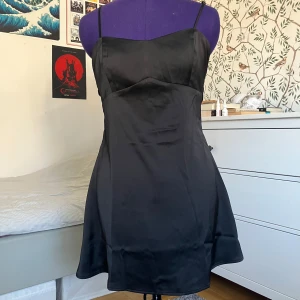 Kort svart klänning - Supersnygg svart klänning i satin från Light Before Dark (köpt på Urban Outfitters). Klänningen har smala axelband och två bredare band som kan knytas till en rosett i ryggen 🎀 Enbart använd en gång och tyvärr för liten