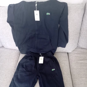 Navy Blue Lacoste set - Svart hoodiejacka från Lacoste med dragkedja framtill och klassisk krokodillogga på bröstet. Jackan har huva med snörning, känguruficka och är tillverkad i mjuk bomull. Perfekt för en chill och sportig look. Den är helt ny då min son beställde fel storlek , man kan köpa en för 600 eller hela set för 1100kr.