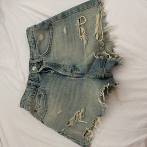 Jeansshorts från Zara - Snygga ljusblå jeansshorts från Zara med råa, fransiga kanter. Shortsen har slitna detaljer och klassisk femficksdesign. Perfekta för sommaren. Den har en fläck vid knapparna, men det syns inte när den är på. Priset kan diskuteras 