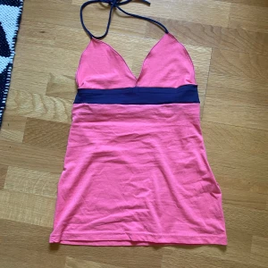 Rosa halterneck linnetopp - Snygg rosa linnetopp med marinblått band under bysten och halterneck-knäppning. Toppen har djup v-ringning och är figurnära med en ärmlös design. Perfekt för varma dagar eller när du vill sticka ut lite extra. Hemmasydd 