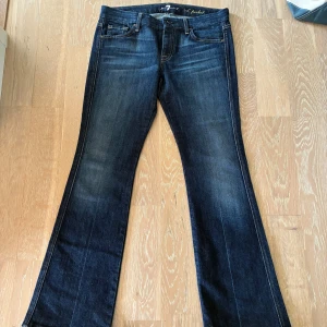 Bootcut jeans från 7 For All Mankind - Mörkblå bootcut jeans från 7 For All Mankind. Jätte fin färg på jeansen. Inga skador förutom att jag har klippt två små hål på insidan av jeansen för att kunna sätta in ett skosnöre (tillkommer inte snöre). Storlek 29, mellan S och M.