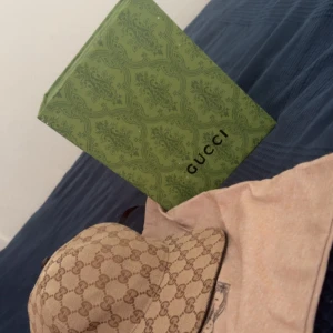 Beige Gucci keps med GG-mönster - Snygg beige keps från Gucci i storlek L, täckt av det klassiska GG-monogrammet. Kepsen har bruna detaljer och justerbart spänne i läder baktill. Tillverkad i bomullsmix och levereras med originalförpackning. Perfekt för dig som vill sticka ut med lyxig streetstyle.