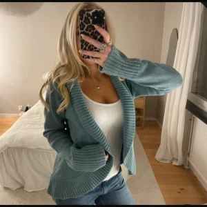 Blå stickad kofta med bred krage - Mysig blå stickad kofta med bred ribbad krage och muddar. Koftan har en loose passform och är perfekt att slänga över en topp. Långärmad och i ett mjukt material som känns skönt mot huden. Enkel att styla till jeans eller kjol.