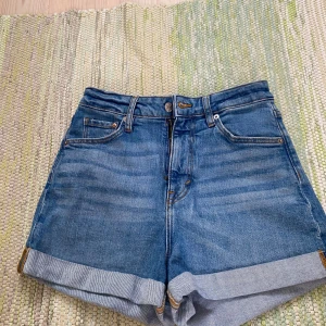 Blå mom jeansshorts från H&M - Snygga blå mom shorts från H&M med ultra hög midja och klassisk femficksdesign. Jeansen har uppvikta benslut och är gjorda i ett mjukt denimtyg. Perfekta för en chill sommarlook med t-shirt eller linne.