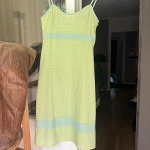 Gulrutigt sommarklänning med smala band - Söt kort klänning med smala axelband i ljusgul och mintgrön rutig bomull. en lätt figurnära passform. Perfekt för varma dagar och ger en fräsch, retroinspirerad look. Från Italien. Säljer eftersom att den var för liten på mig.